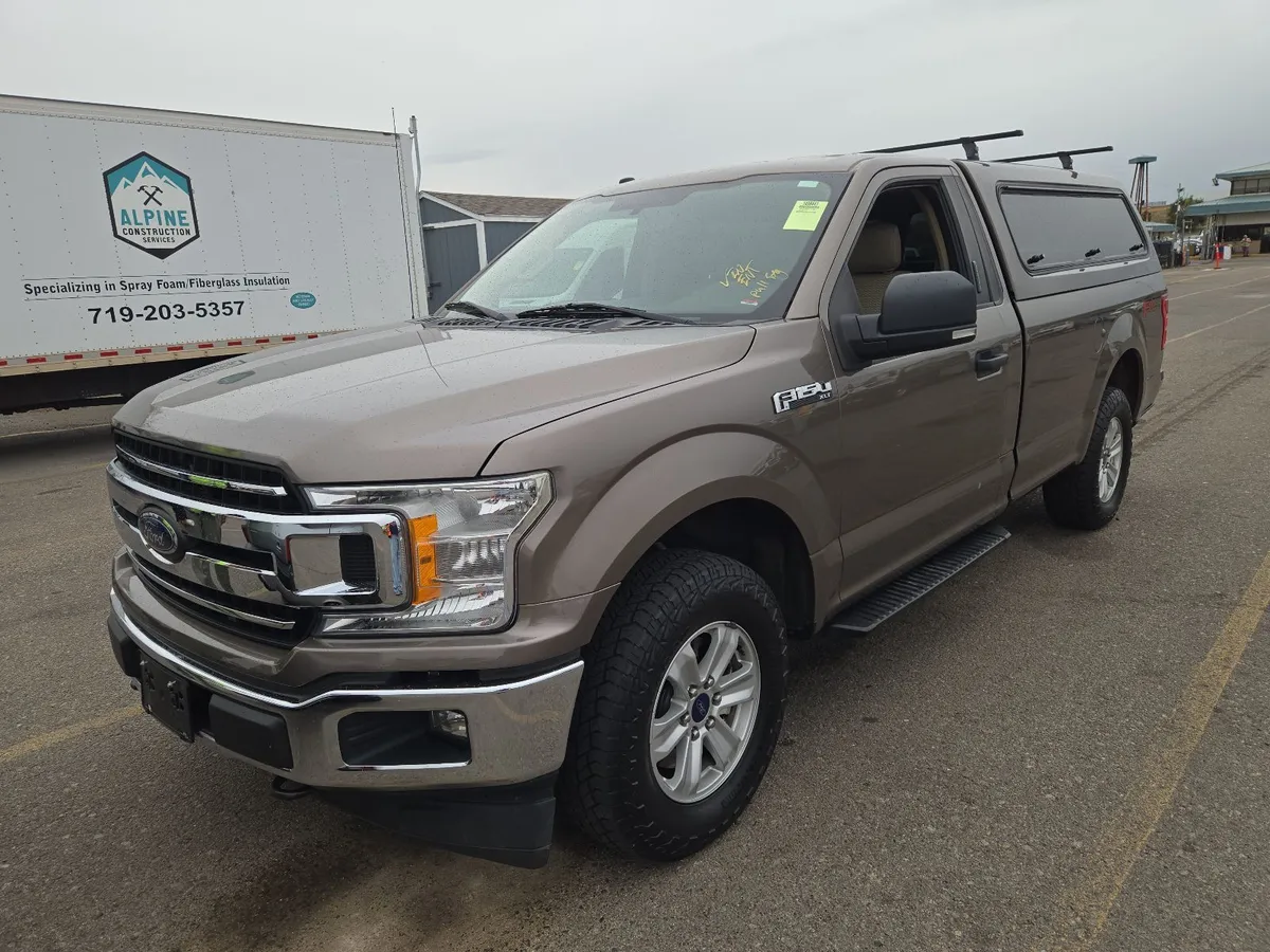 2018 Ford F-150 XLT regular cab in bronze with a matching camper shell and roof rack, front three-quarter view on the auction lot