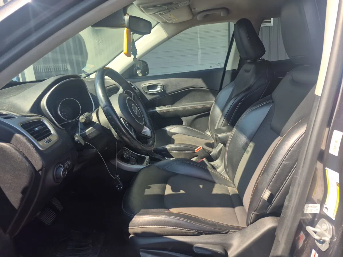 Interior of the 2017 Jeep Compass Latitude showing black leather-trimmed seats, a worn steering wheel and a dusty dash
