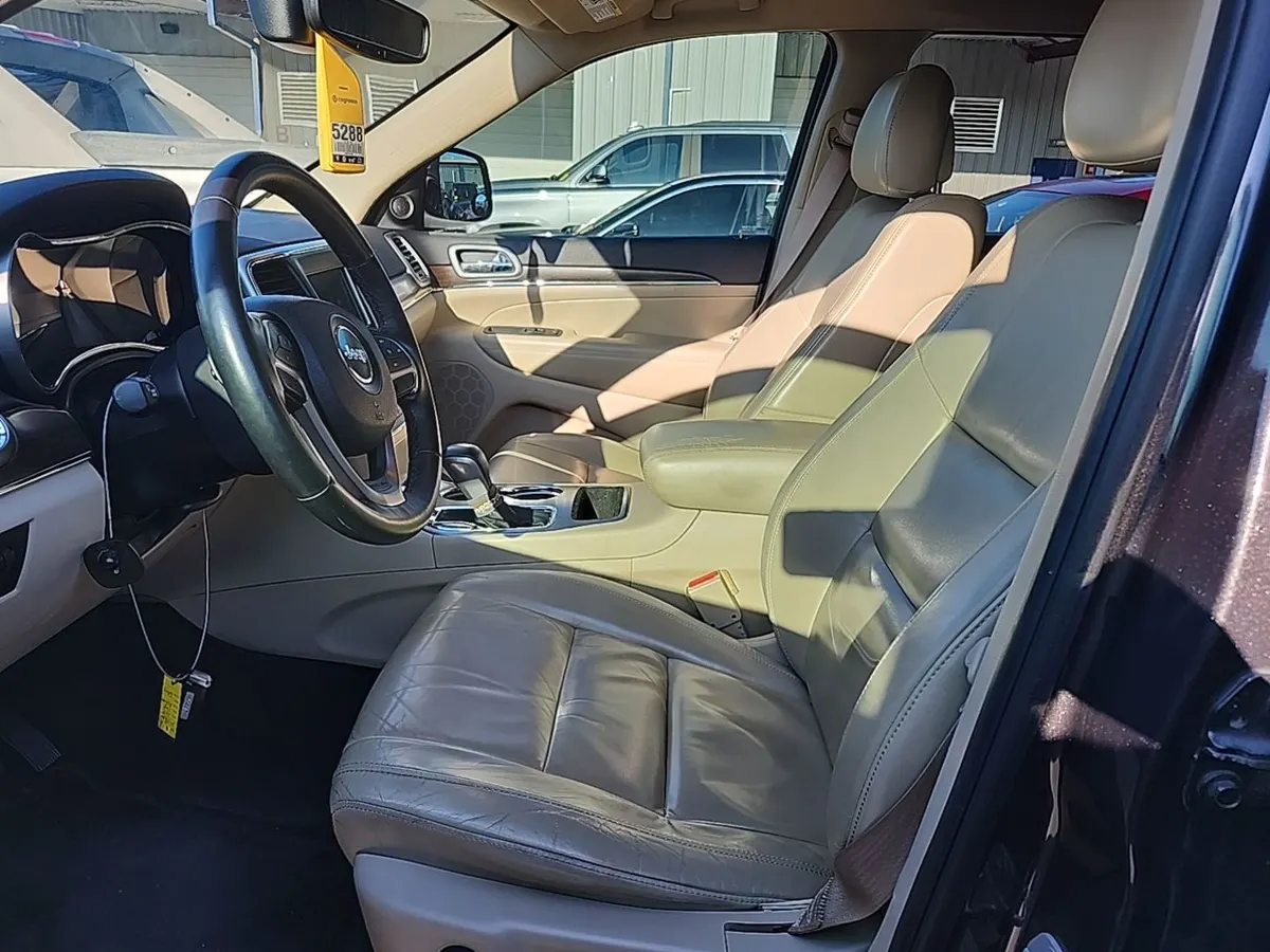 Interior of the 2018 Jeep Grand Cherokee Limited with tan leather seats showing wear on the driver's side bolster
