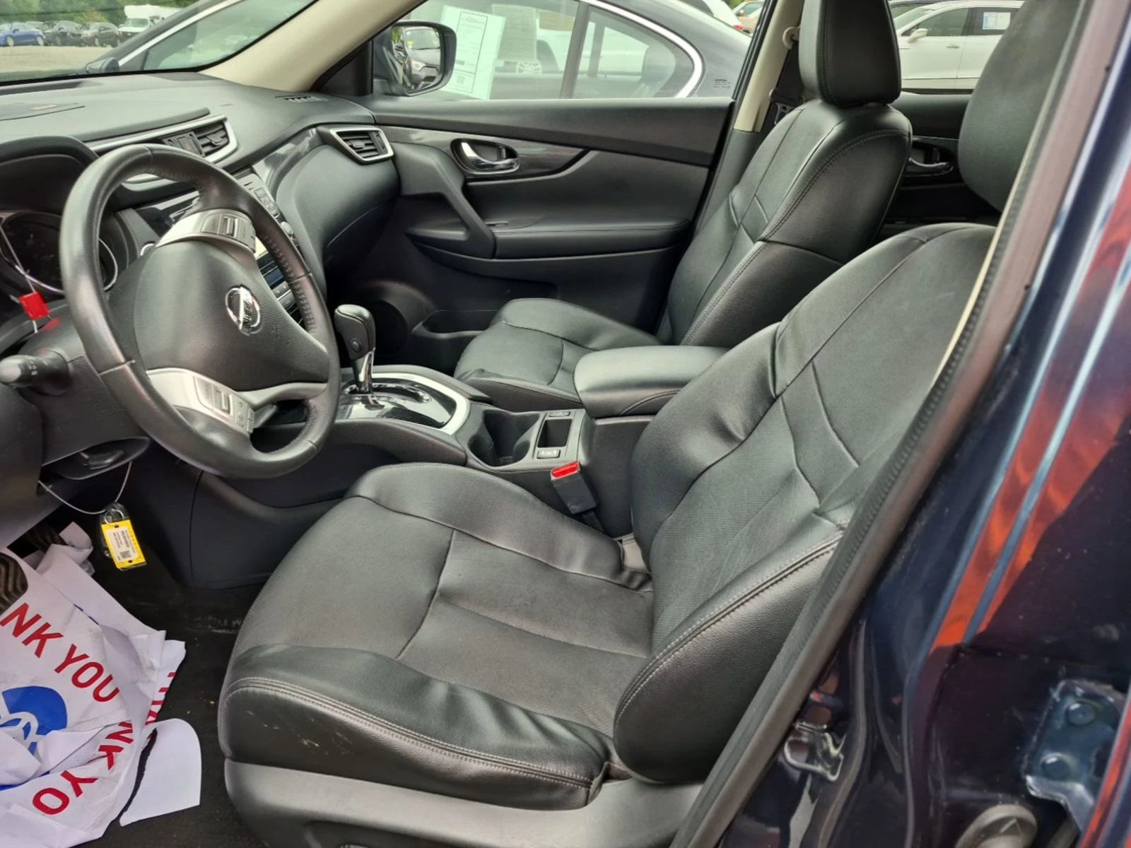 Interior of the 2016 Nissan Rogue SL showing clean black leather front seats, leather-wrapped steering wheel, and center console