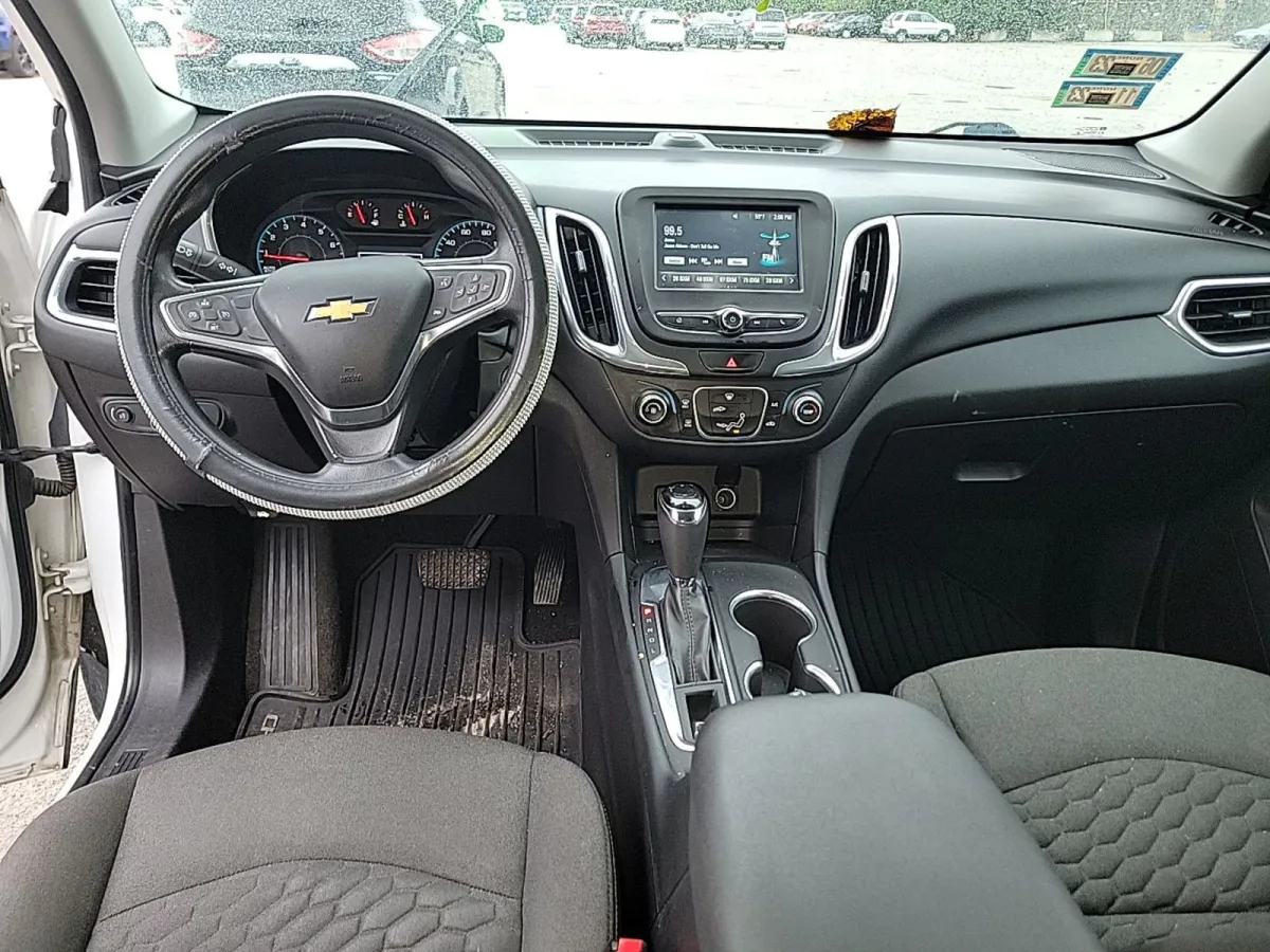 Interior of the 2018 Chevrolet Equinox LT showing black cloth seats, a worn aftermarket steering wheel cover, and dirty rubber floor mats